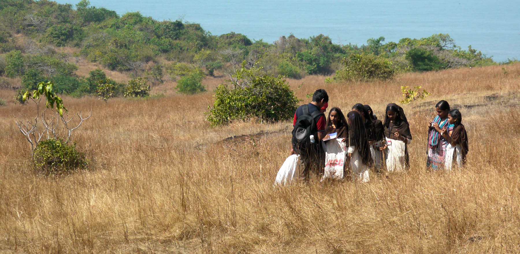 A facilitator and students pausing on coastal grassland during a nature-walk field programme, estuary and sea behind them